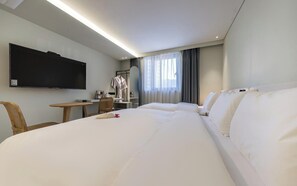 Habitación de hotel con una cama grande, televisor montado en la pared, escritorio con una silla y ventana con cortinas.