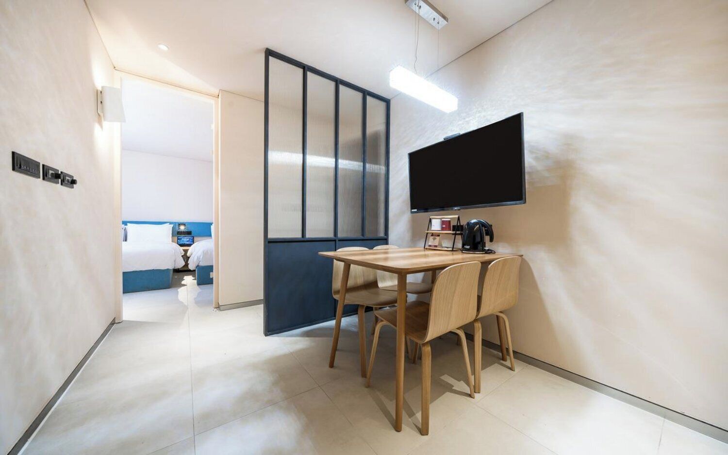 Habitación de hotel con cama, escritorio con sillas, televisión de pantalla plana y puerta corredera que da a otra habitación.