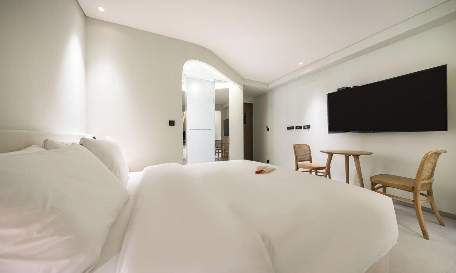 A hotel room with a large bed, a TV mounted on the wall, a small table, and two chairs.