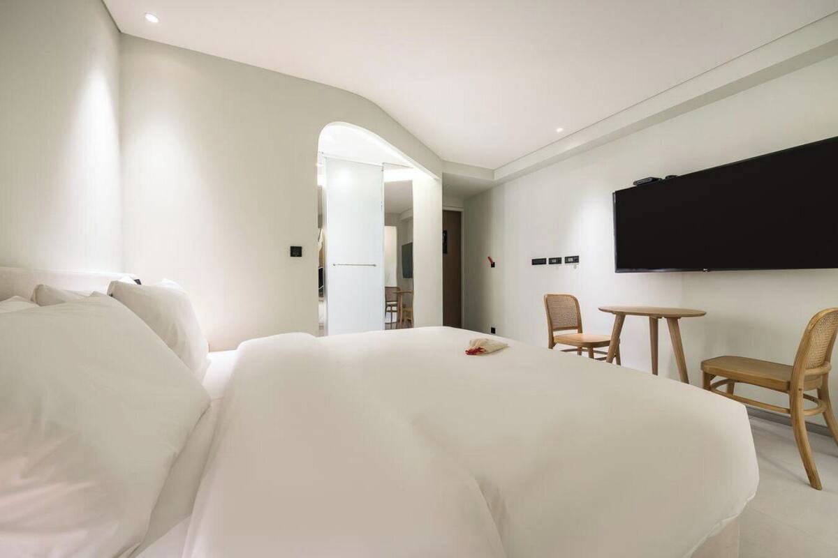 Una habitación de hotel con una cama grande, un televisor montado en la pared, una mesita pequeña y dos sillas.