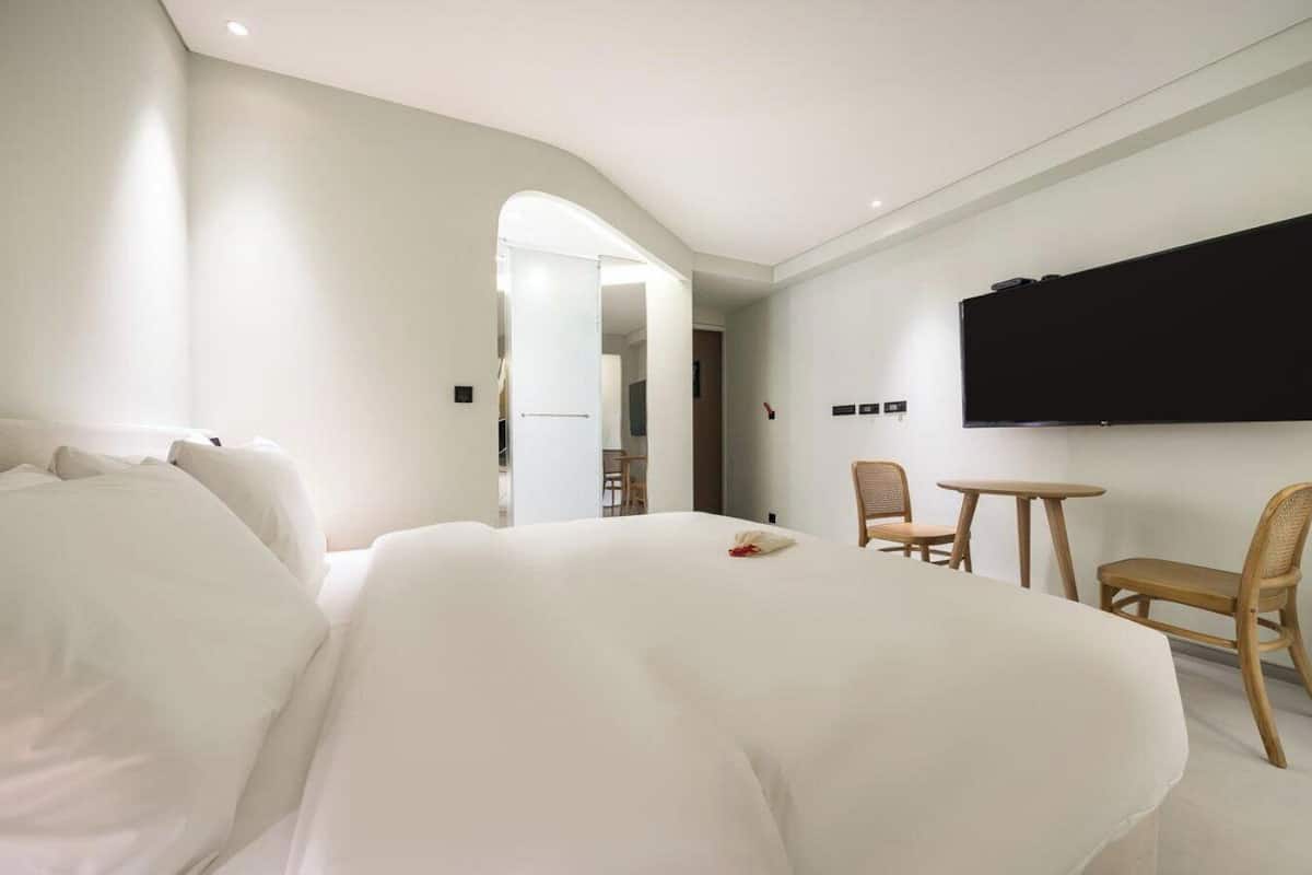 A hotel room with a large bed, a TV mounted on the wall, a small table, and two chairs.
