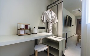 Una habitación de hotel moderna con un escritorio blanco, una bata colgada en un perchero, una cafetera y una silla.