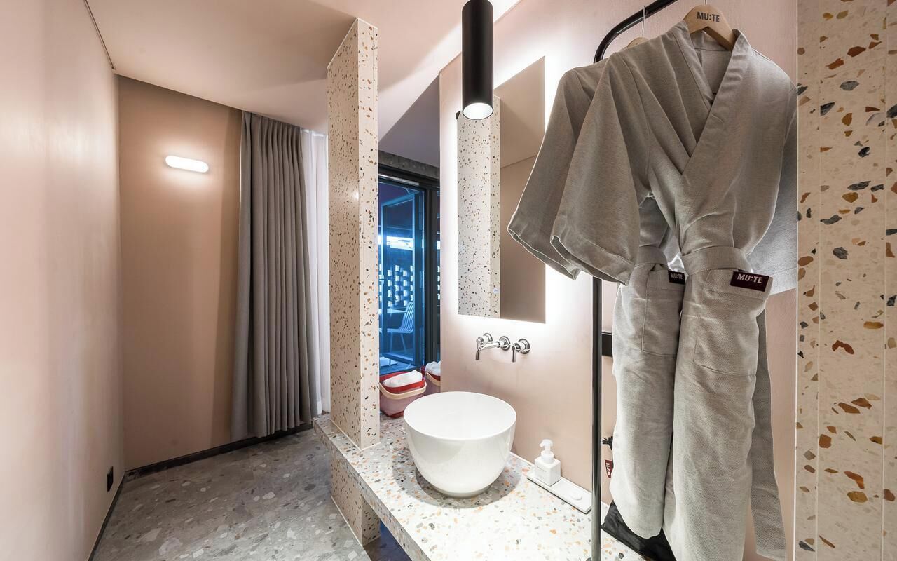 A modern bathroom with a large mirror, a sink, and a robe hanging on a rack.