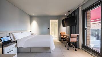 Una habitación de hotel moderna con una cama grande, un escritorio con una computadora portátil, un televisor y una ventana con vistas.