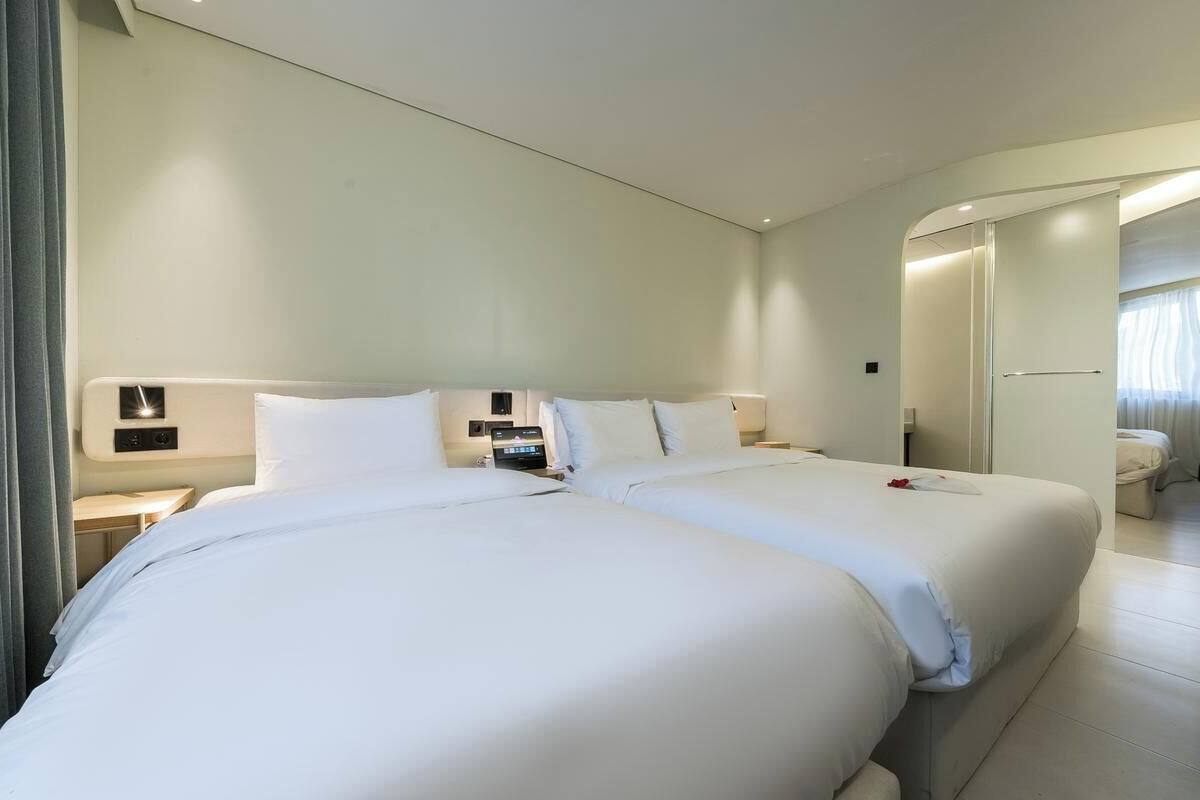 Habitación de hotel con dos camas, una mesita de noche, un espejo y un baño visible a través de una puerta abierta.