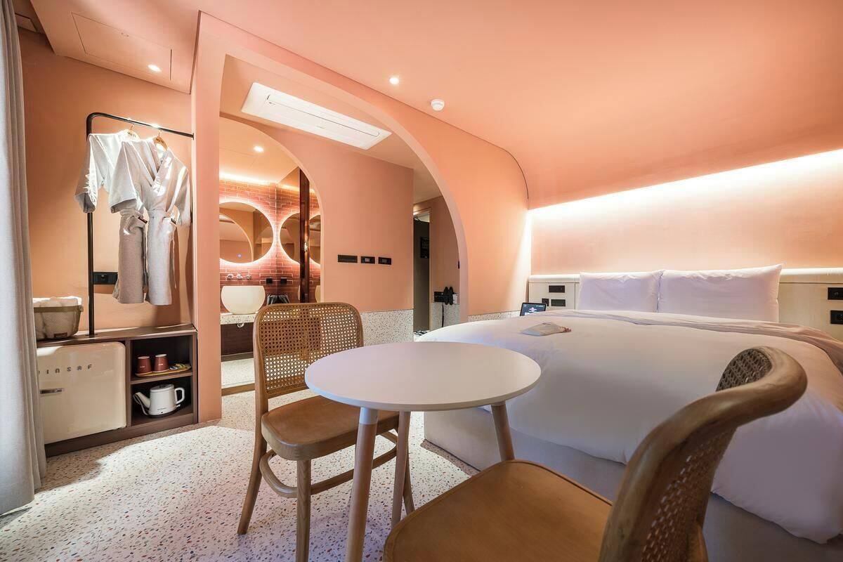 Habitación de hotel con cama, una mesa, sillas, tocador con espejo y perchero.