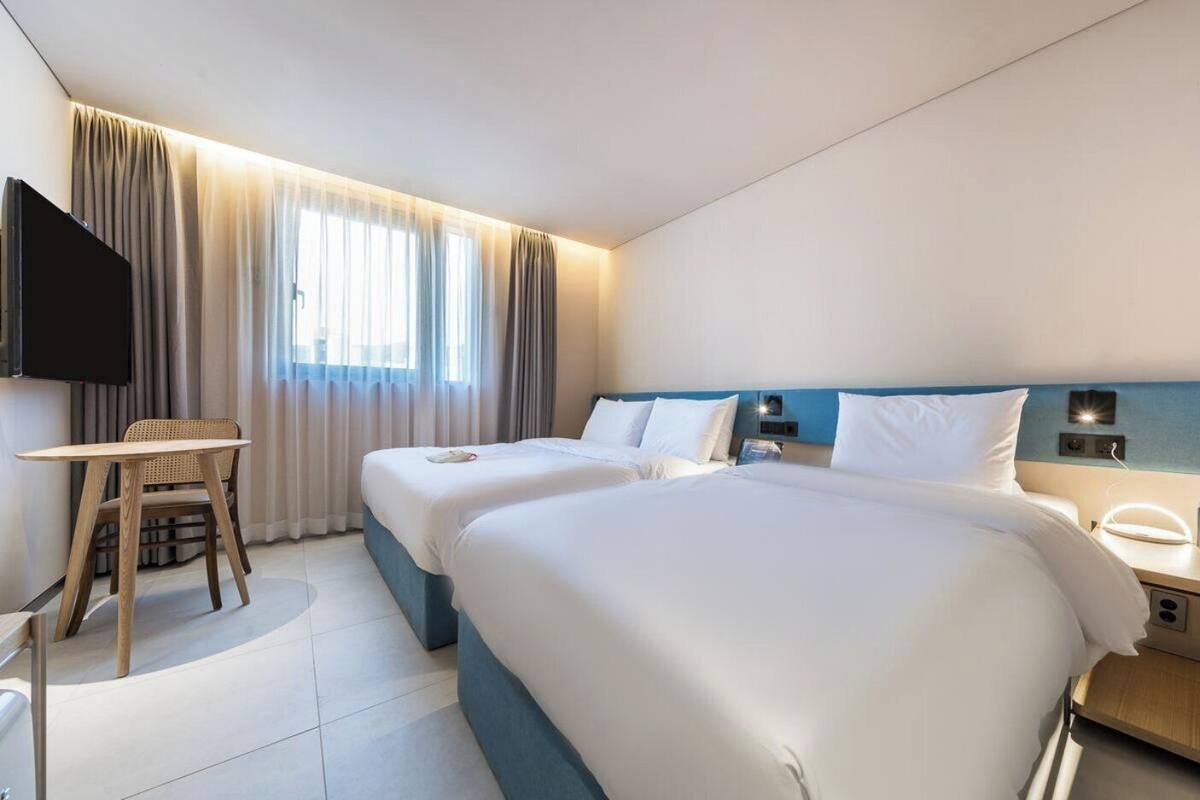 Una habitación de hotel con dos camas, un escritorio, una silla, un televisor y una ventana con cortinas.