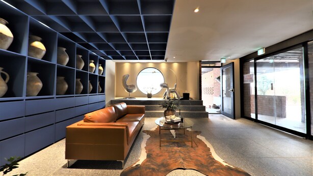 Een moderne lobby met een leren bank, een glazen salontafel en een opvallende wanddecoratie van vazen.