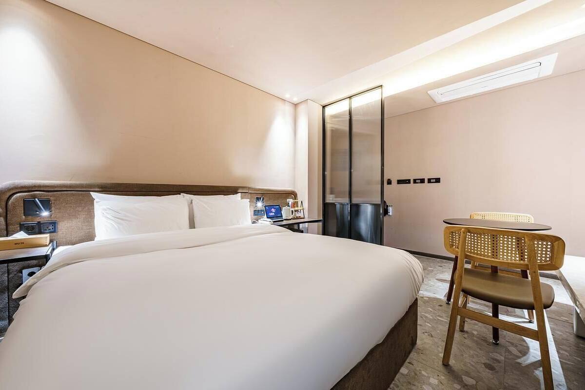 Habitación de hotel con una cama grande, un escritorio con silla, un espejo y un aire acondicionado de pared.