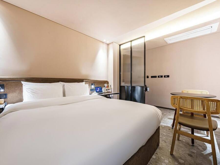 Habitación de hotel con una cama grande, un escritorio con silla, un espejo y un aire acondicionado de pared.