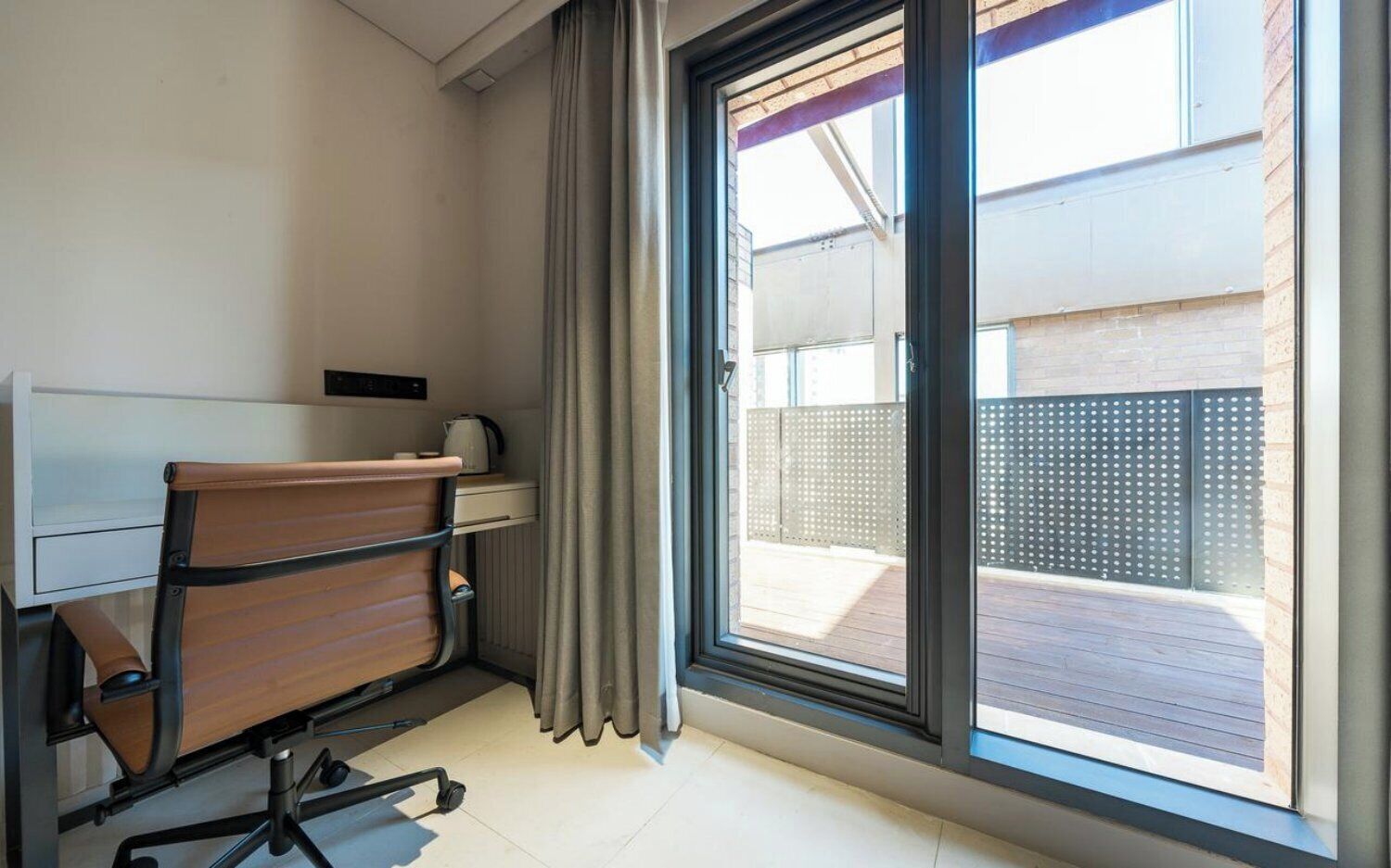 A compact room with a desk, chair, and a large sliding glass door leading to an outdoor deck.