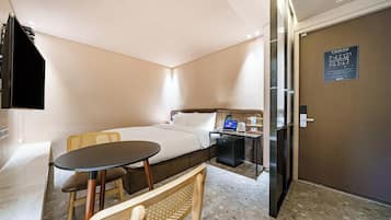 Une chambre d’hôtel avec un lit, une petite table, une chaise, un bureau avec un ordinateur portable et une porte avec une pancarte.