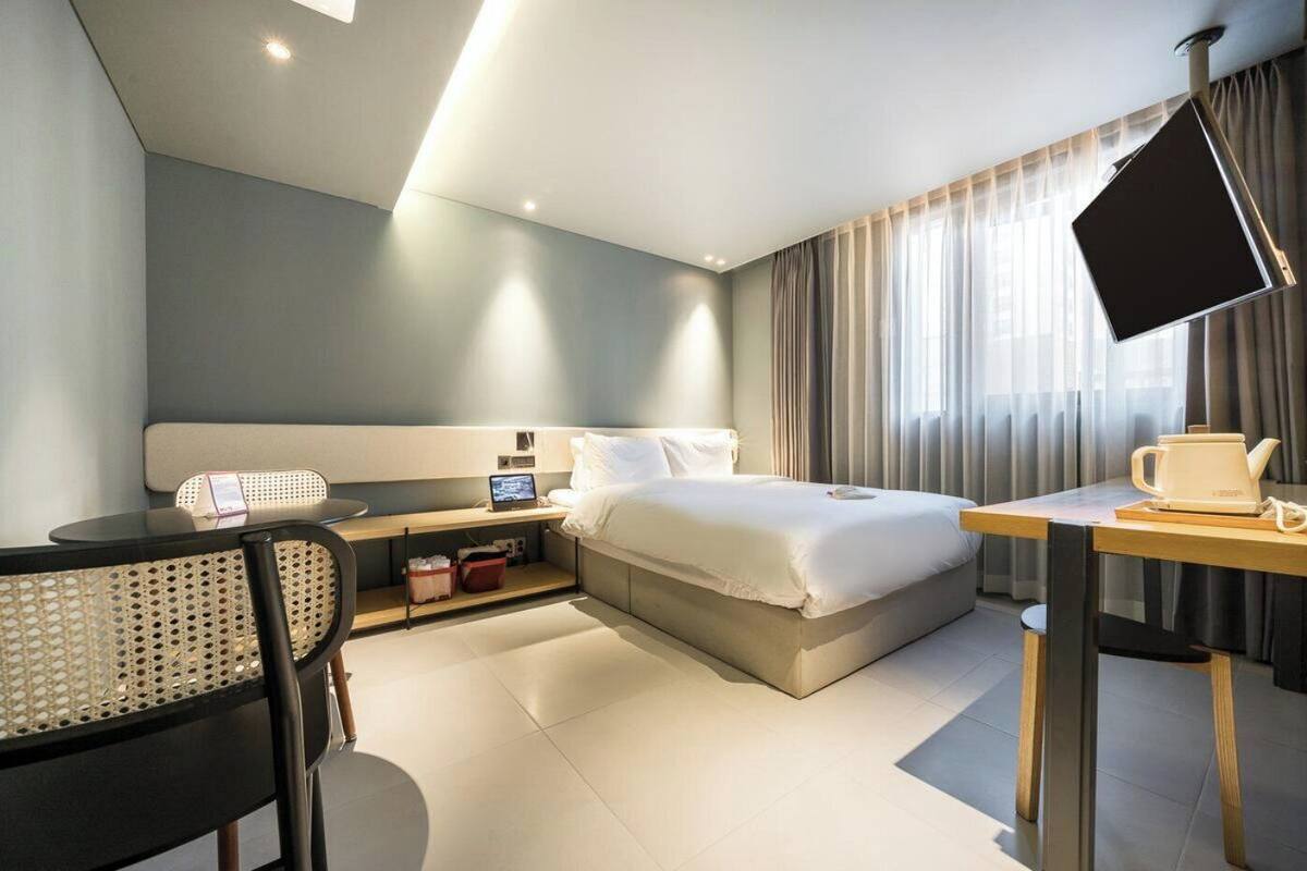 Una habitación de hotel moderna con cama, escritorio, silla y un ventanal con cortinas.