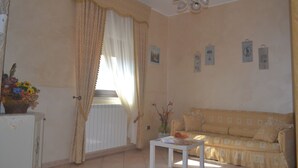 Un salón con un sofá beige, una mesa de centro blanca y una ventana con cortinas.