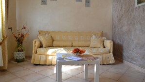 Una sala de estar con un sofá estampado, una mesita con un florero y una revista, y una pared decorativa con tres objetos enmarcados.