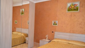 Un dormitorio con dos camas, una mesita de noche, un espejo y una pared decorada con motivos florales.