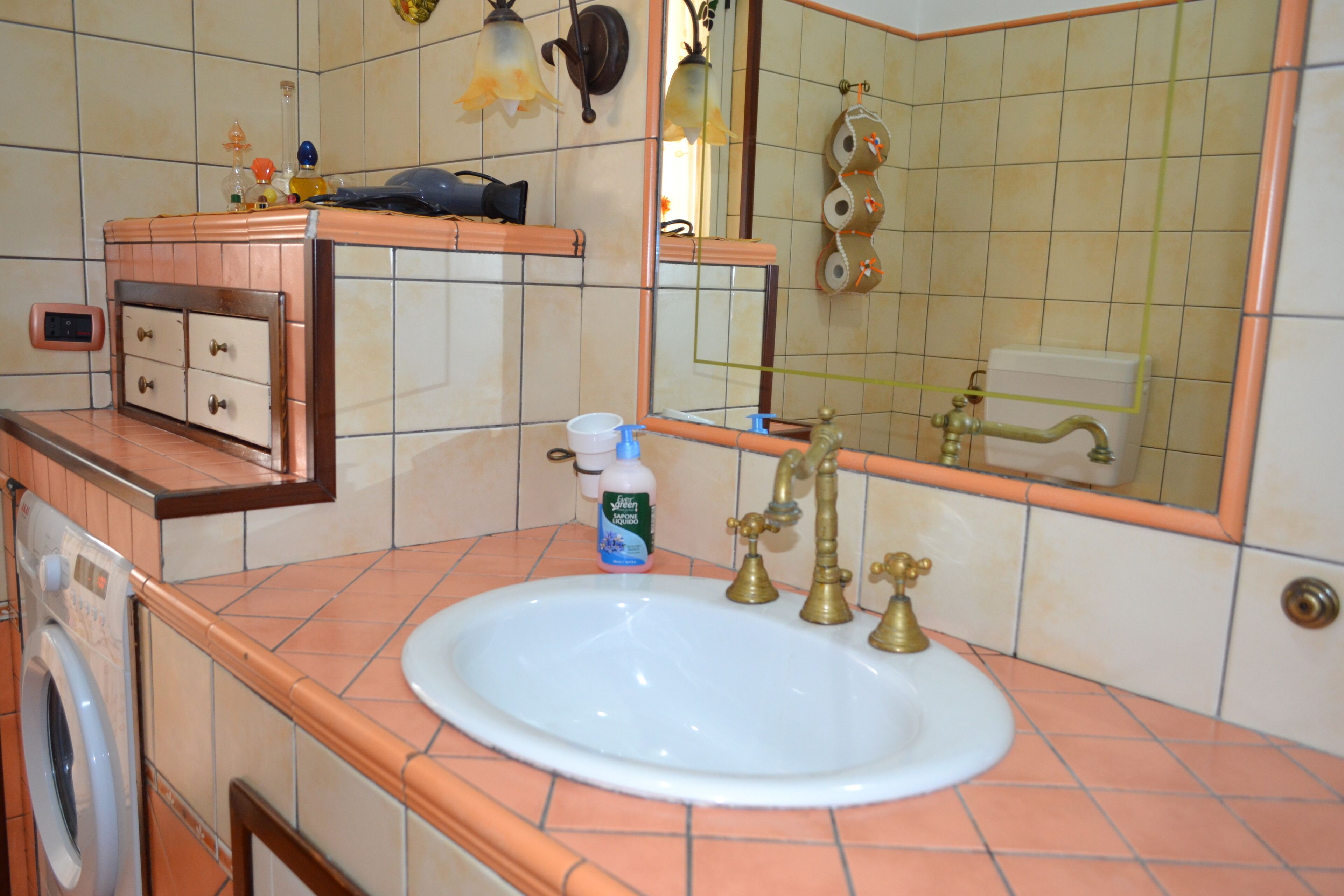 Ein Badezimmer mit einem weißen Waschbecken, einem Spiegel, einem Handtuchhalter und einer Waschmaschine.