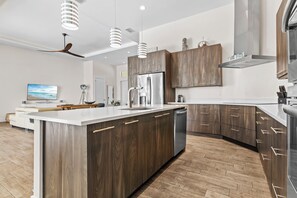 A modern kitchen with a central island, wooden cabinets, stainless steel appliances, and pendant lighting. - Intervillas Florida - Villa Leonardo (Cape Coral)
