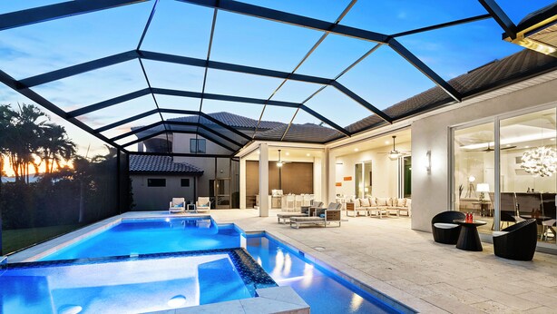 A modern outdoor pool area with a glass ceiling, lounge seating, and a well-lit interior space. - Intervillas Florida - Villa Leonardo (Cape Coral)