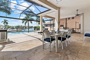 A spacious outdoor dining area with a pool view, a covered seating area, and a brick wall. - Intervillas Florida - Villa Leonardo (Cape Coral)