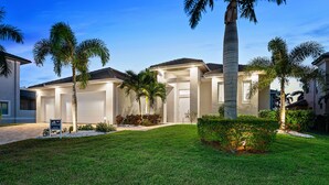 A modern two-story house with a well-maintained lawn, palm trees, and a garage. - Intervillas Florida - Villa Leonardo (Cape Coral)