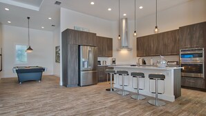 A modern kitchen with a central island, bar stools, a built-in oven, and a pool table. - Intervillas Florida - Villa Leonardo (Cape Coral)