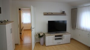 A living room with a flat-screen TV on a wooden stand, a white cabinet, and a door leading to another room. - Apartment Julius 1 - nice, quiet and right in the middle - (Sankt Andreasberg)