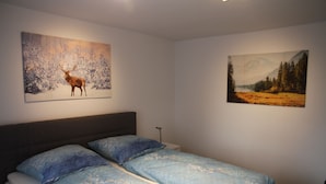 A bedroom with a bed, two pillows, and two wall-mounted paintings. - Apartment Julius 1 - nice, quiet and right in the middle - (Sankt Andreasberg)