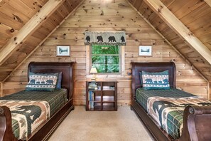 Cozy attic bedroom with two single beds, a nightstand, and a window with a view.