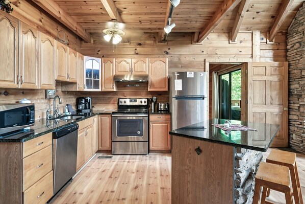A wooden cabin kitchen with a central island, stainless steel appliances, and a stone wall.