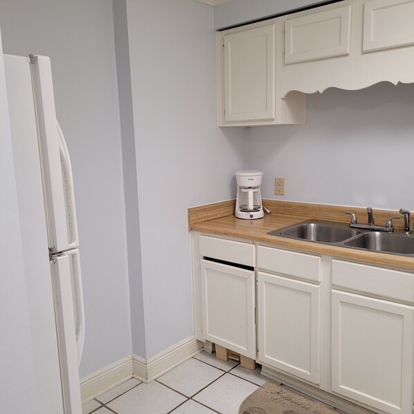 A compact kitchen with white cabinets, a stainless steel sink, and a white coffee maker.