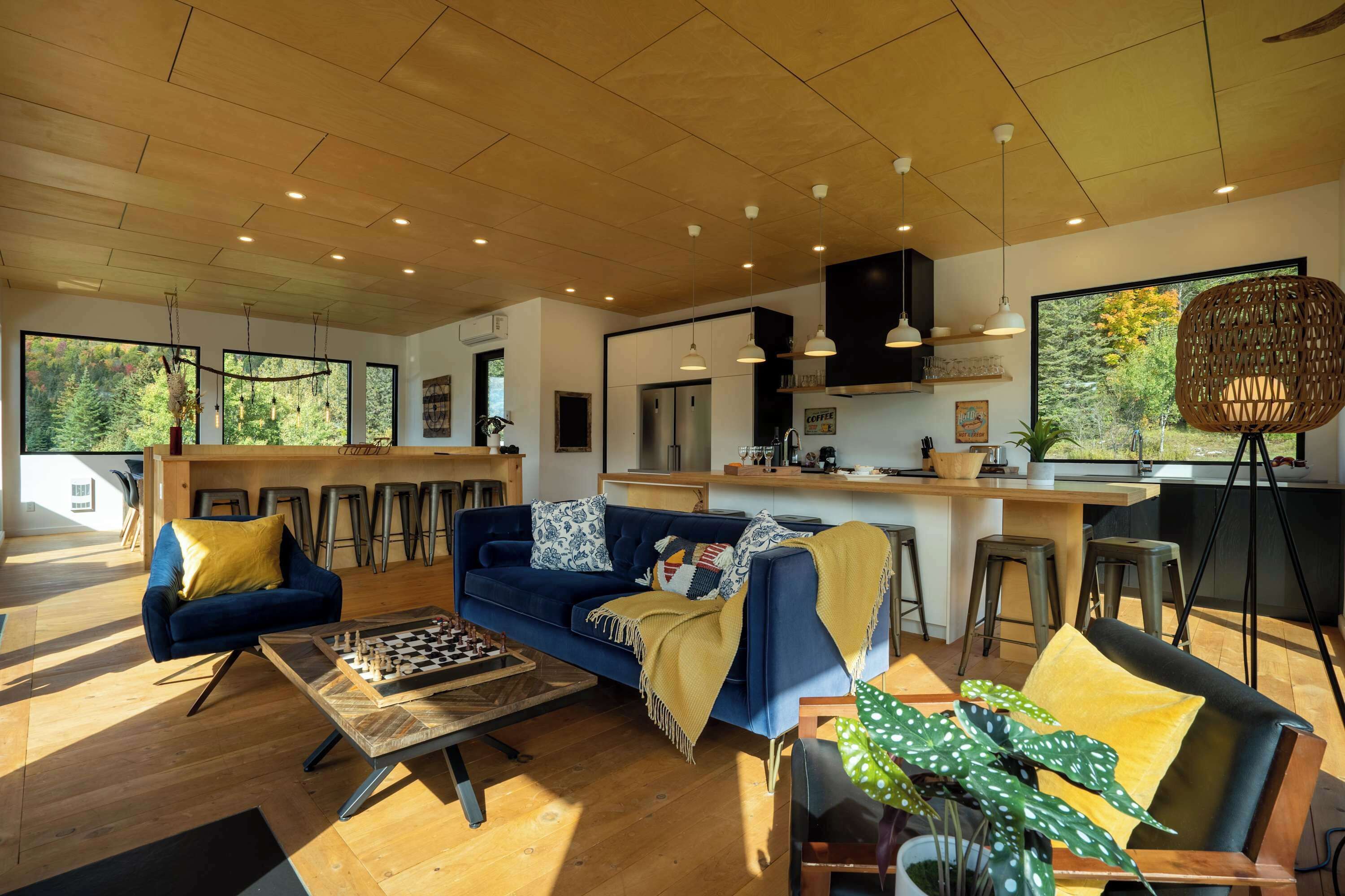 A modern living room with a blue sofa, wooden coffee table, and a large window offering a view of trees.