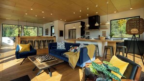 A modern living room with a blue sofa, wooden coffee table, and a large window offering a view of trees.