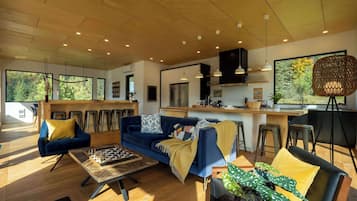 A modern living room with a blue sofa, wooden coffee table, and a large window offering a view of trees.