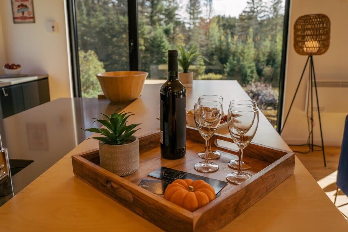 Una mesa de comedor con una bandeja de madera, una botella y copas de vino.