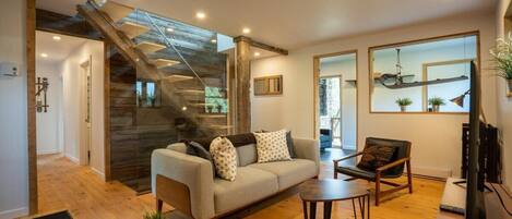 A modern living room with a sofa, coffee table, and chairs. A staircase with wooden accents leads to another level.