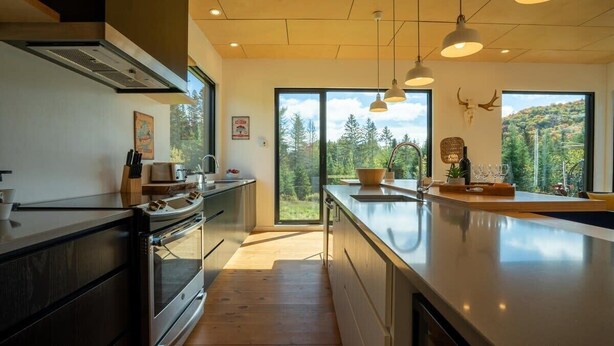 A modern kitchen with a large island, wooden flooring, and pendant lighting.