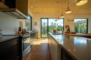 A modern kitchen with a large island, wooden flooring, and pendant lighting. - Lakeside Trails, Heated Spa & Ski Adventures (Sainte-Lucie-des-Laurentides)