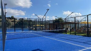 Una cancha de tenis con superficie azul, rodeada por una valla negra y equipada con múltiples focos.