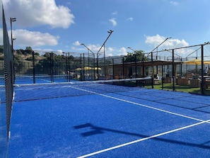 A tennis court with a blue surface, surrounded by a black fence, and equipped with multiple floodlights.