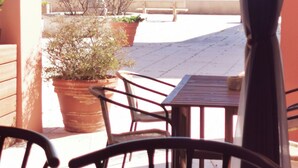 Un patio al aire libre con mesa y sillas, plantas en macetas y vista al mar.