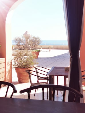 An outdoor patio with a table and chairs, potted plants, and a view of the sea.
