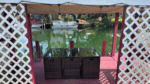 A covered outdoor seating area with wicker furniture, a wooden deck, and a view of a water body with boats. - Newly Remodeled Weeki Wachee River Retreat (Spring Hill)