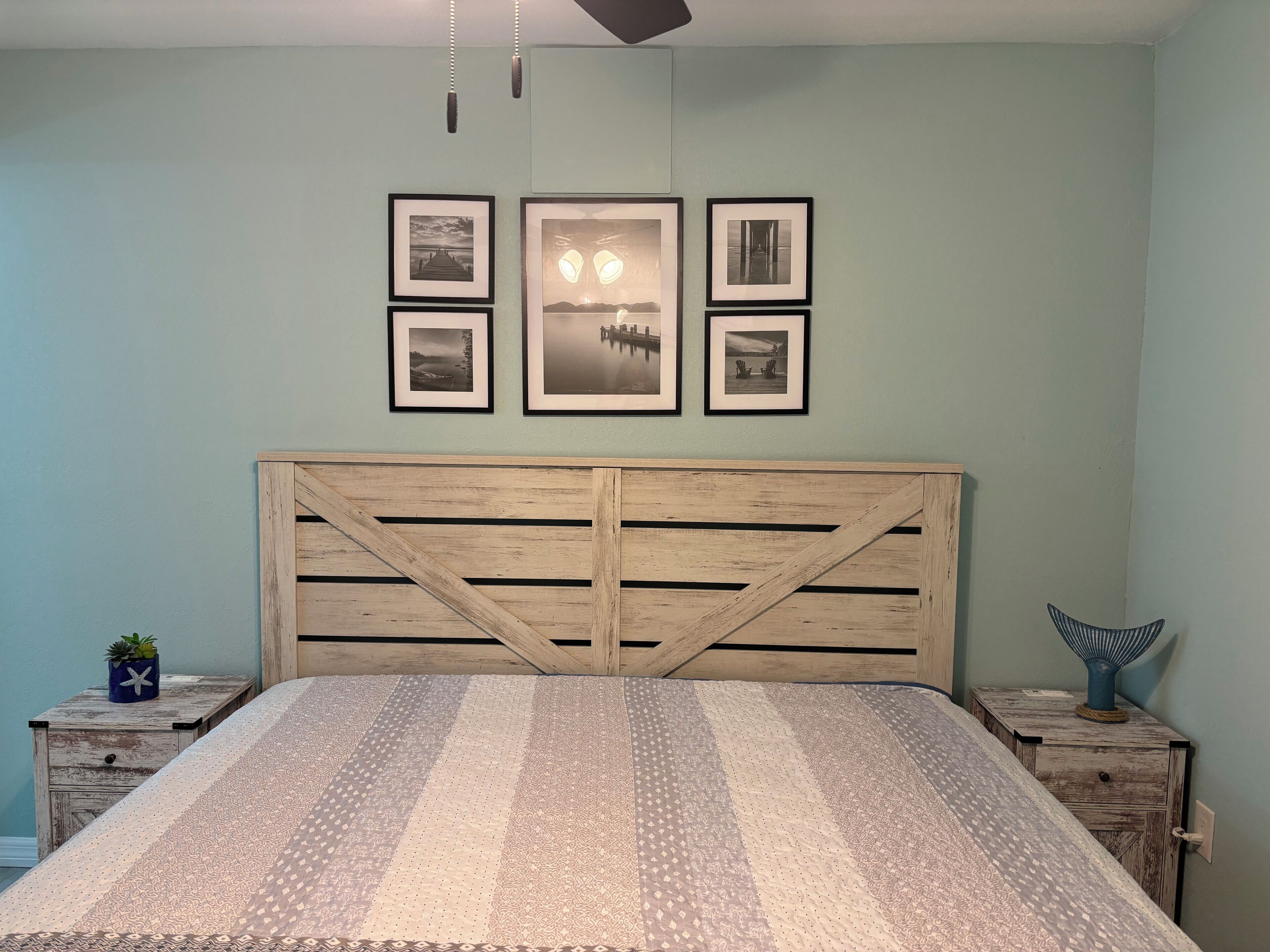 A bedroom with a wooden headboard, a patterned bedspread, and four framed pictures on the wall.