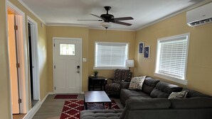 A living room with a gray sectional sofa, a red patterned rug, a ceiling fan, and a door with a window. - Newly Remodeled Weeki Wachee River Retreat (Spring Hill)