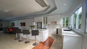 A modern kitchen with white cabinets, a central island with bar stools, and a large window providing natural light. - Luxury 5BD Villa - Massive Pool & Outdoor Vibe (Gros Islet)