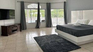 A modern bedroom with a large bed, a flat-screen TV, and a view of a pool and outdoor area. - Luxury 5BD Villa - Massive Pool & Outdoor Vibe (Gros Islet)
