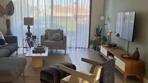 A modern living room with a sofa, coffee table, and a TV mounted on the wall. - Bright, Stylish Desert Condo with Mountain Views + Private Courtyard (Rancho Mirage)