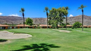 A golf course with a clear view of the surrounding landscape, including mountains and a row of buildings with red-tiled roofs. - Bright, Stylish Desert Condo with Mountain Views + Private Courtyard (Rancho Mirage)