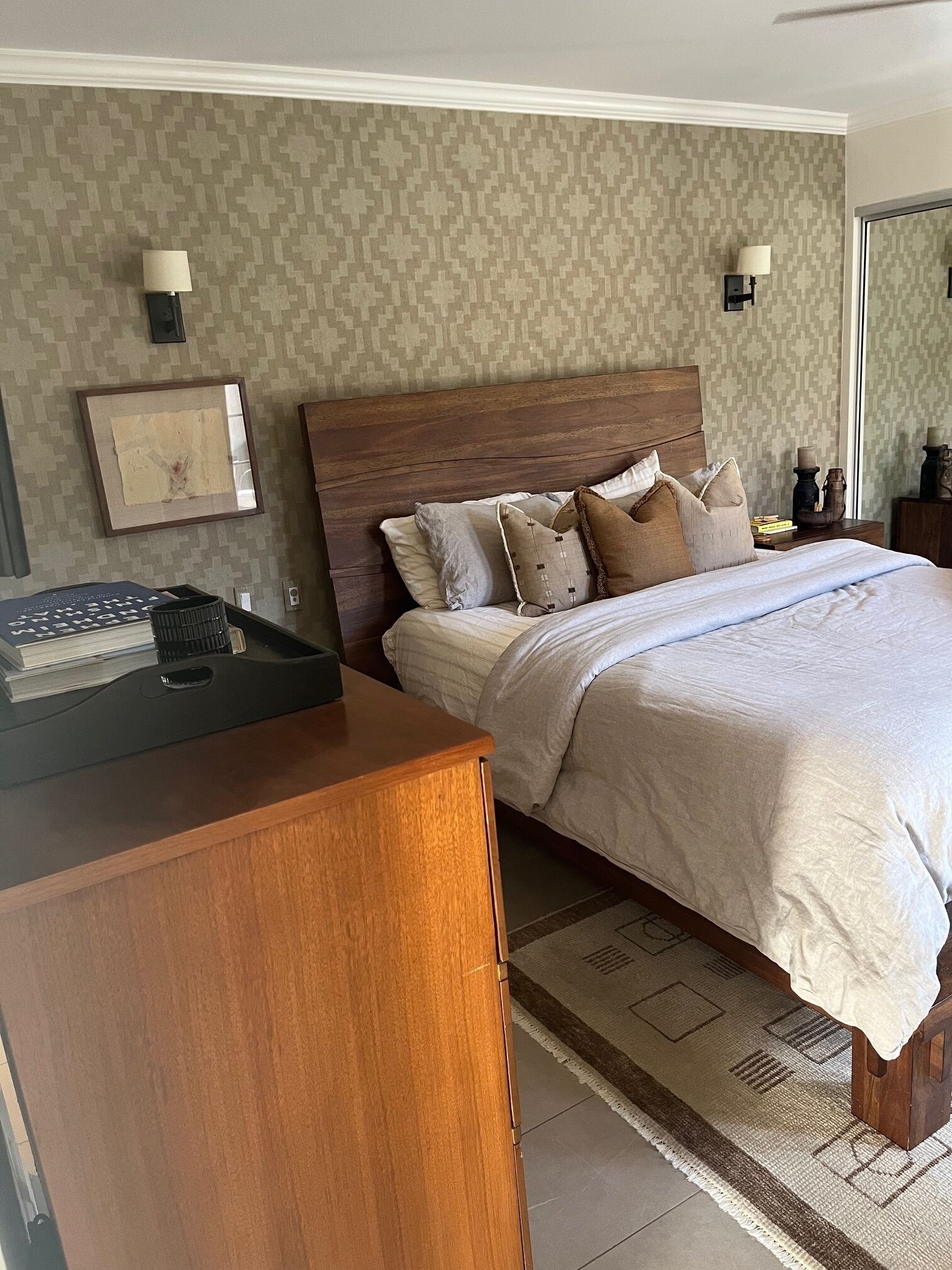 A neatly arranged bedroom with a wooden headboard, a bed with multiple pillows, a bedside table, and a nightstand with a lamp.